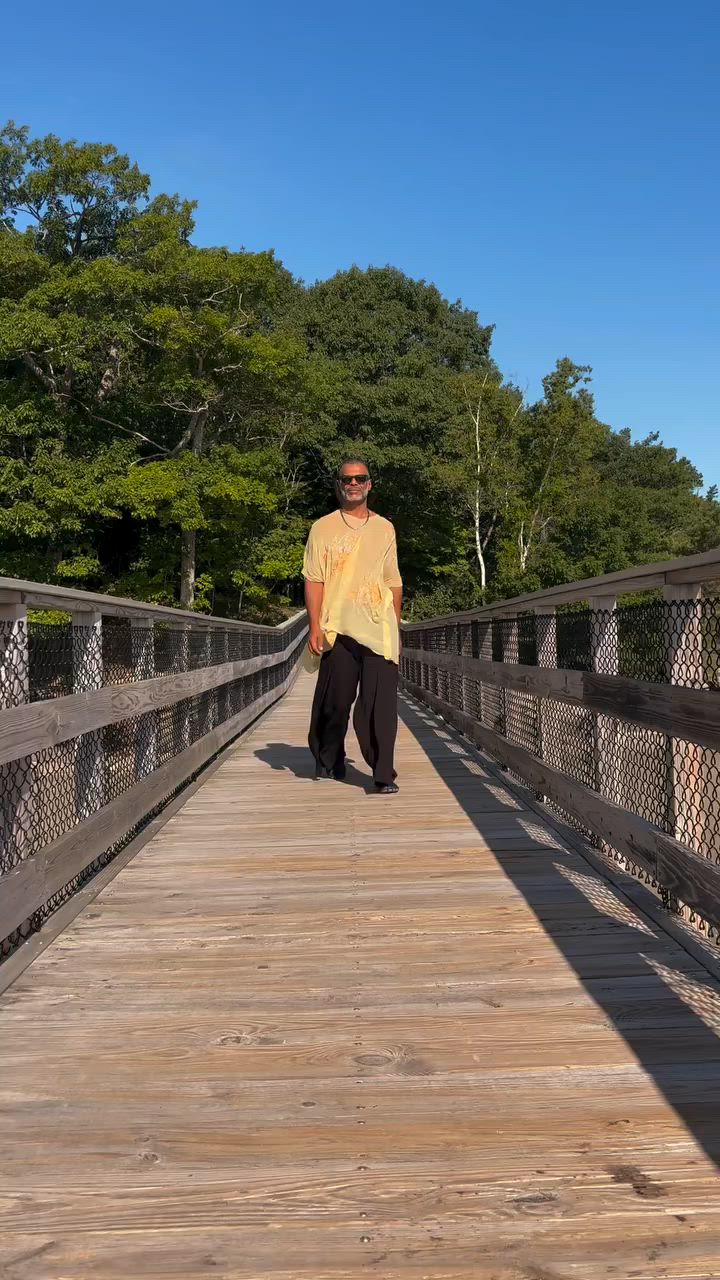 Still from Kristopher’s lemon-party Reel, wearing a pale yellow handmade top and dark trousers on a wooden bridge.
