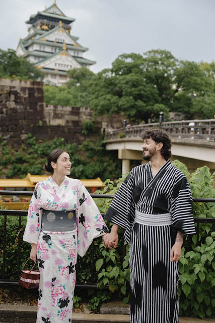 Couple in traditional Japanese attire holding hands near Osaka Castle