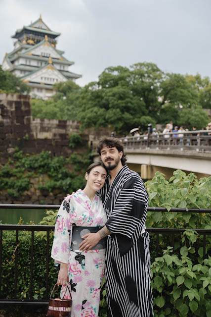 Couple in floral and striped yukata robes standing before Osaka Castle