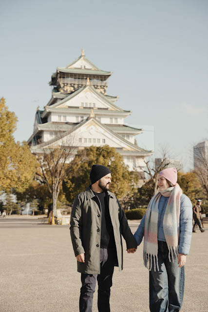 Couple holding hands in front of Osaka Castle wearing winter coats and beanies