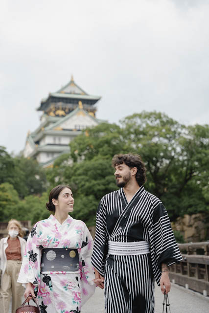 Couple in traditional yukata walking hand in hand with Osaka Castle in background