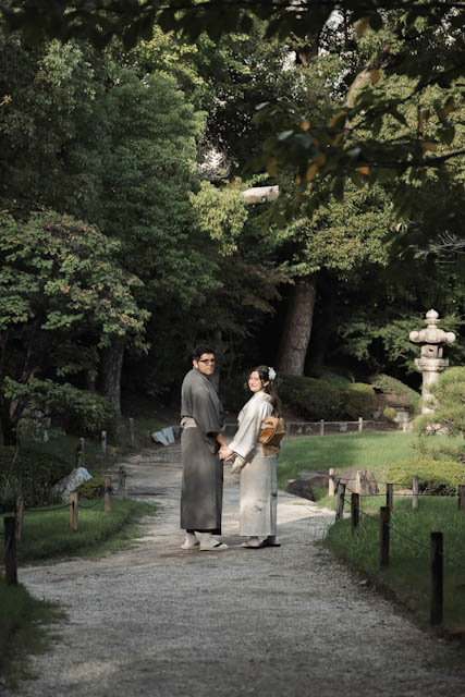 Couple in traditional kimonos holding hands on a gravel path in a Japanese garden