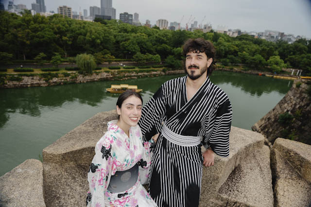 Couple in traditional kimonos posing on a stone wall overlooking a moat