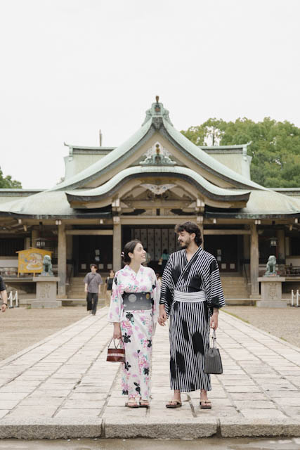 Couple in traditional yukata holding hands in front of a Japanese shrine