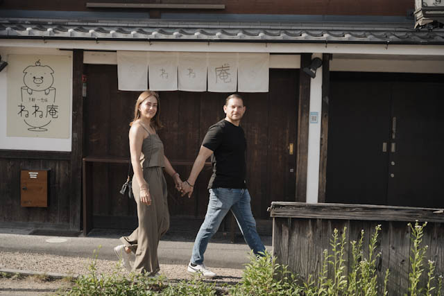 Couple holding hands walking past a traditional Japanese building with a pig logo sign