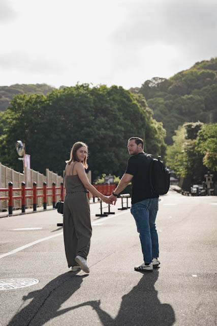 Couple holding hands and looking back while walking on a road near a shrine
