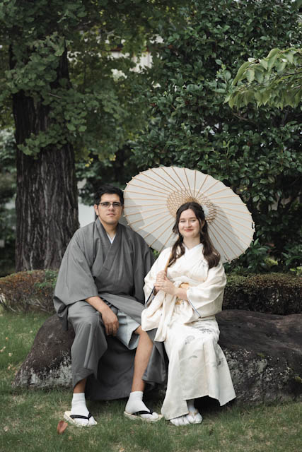 Couple in traditional kimono sitting on a rock with a paper umbrella in a garden