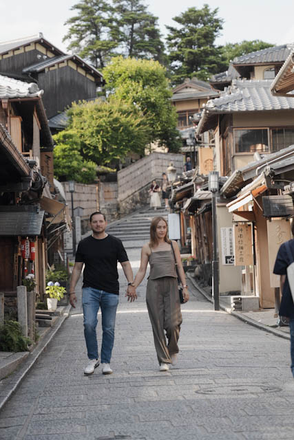 Couple holding hands walking down a historic stone street with traditional Japanese buildings