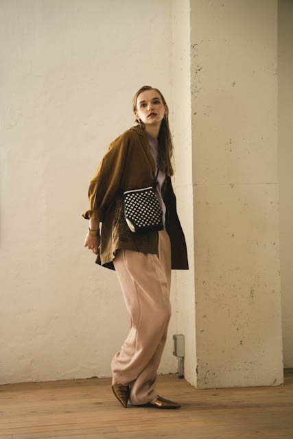 Woman in mustard jacket and pink trousers posing against a textured white wall