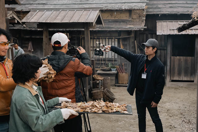 Film crew filming a scene with a clapperboard in a rustic village setting