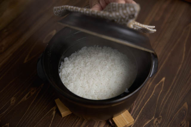 黒い土鍋に入った炊き立てのご飯と木製のテーブル