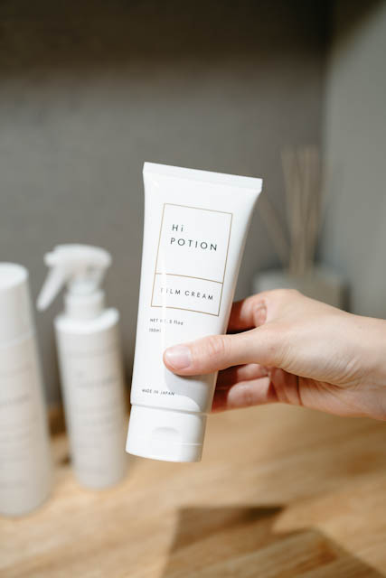 Hand holding a white Hi Potion film cream tube with other skincare products in the background.