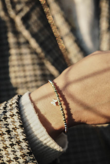 Wrist wearing gold bracelet and star charm against textured fabric