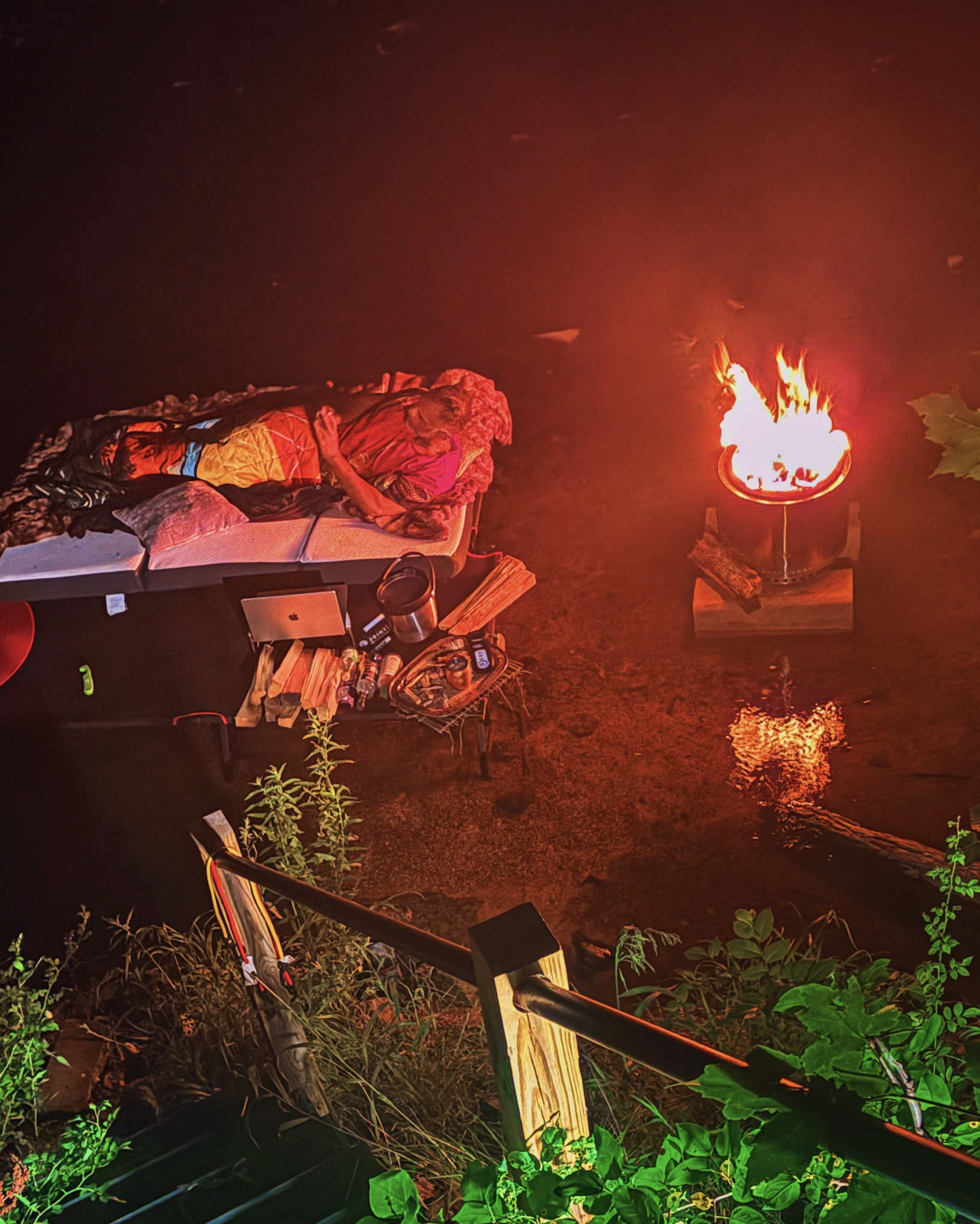 An outdoor lounge arranged beside a fire and screen in the trees.