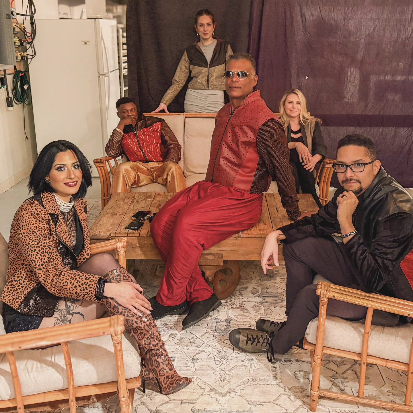 Kristopher in red leather with fellow creatives in an ornate room.