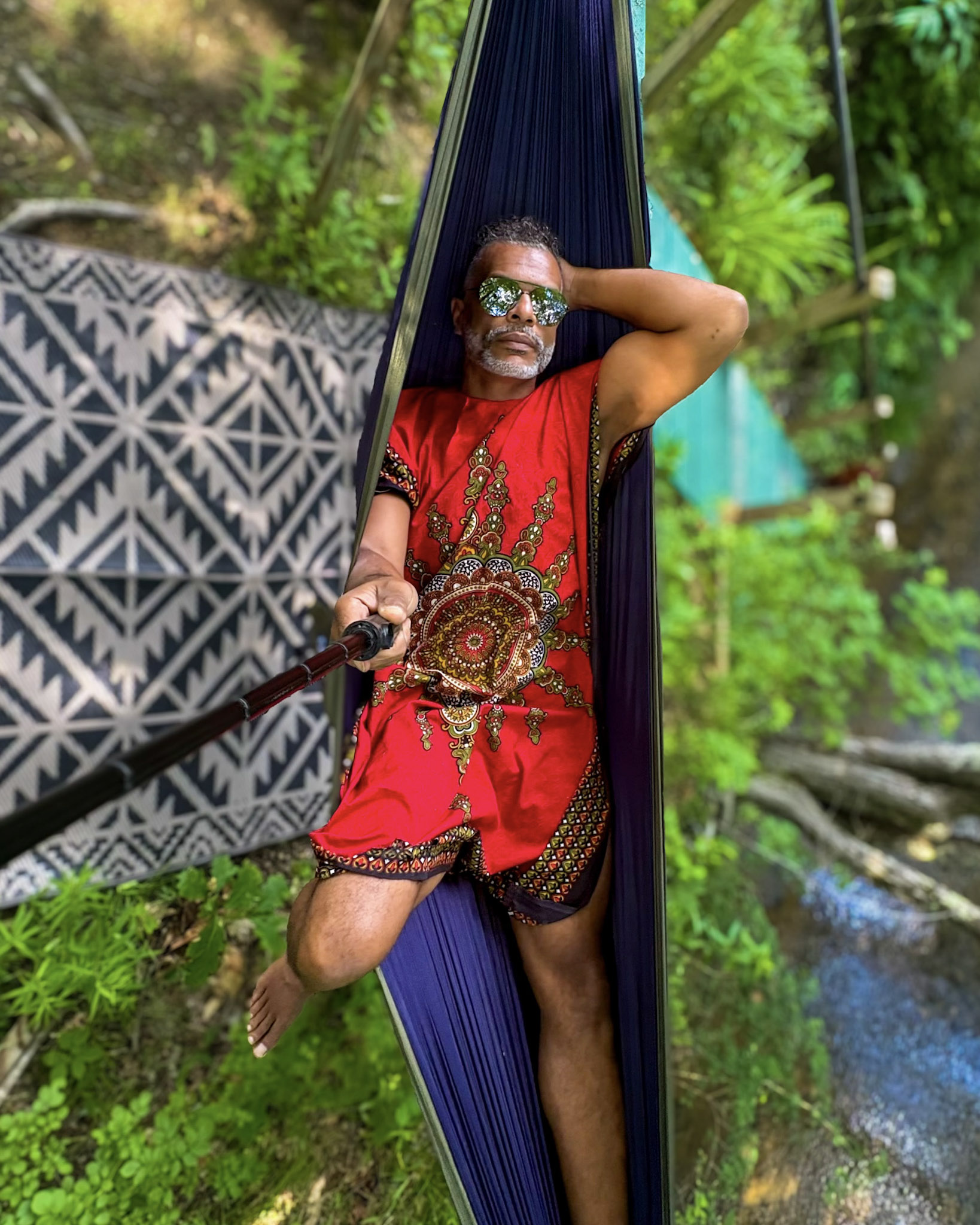 Kristopher wearing a red patterned dashiki beside an outdoor hammock.