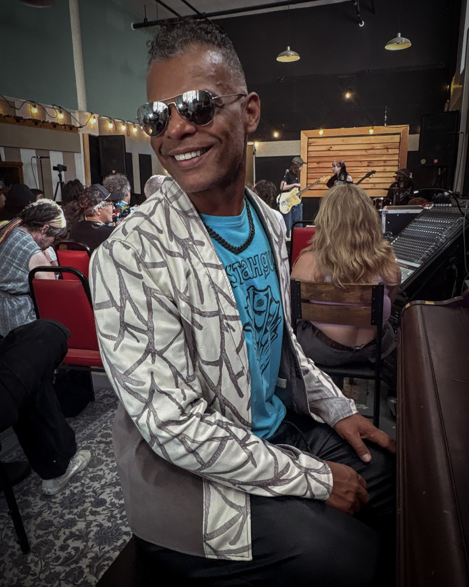 Kristopher in a white patterned jacket at a music venue.