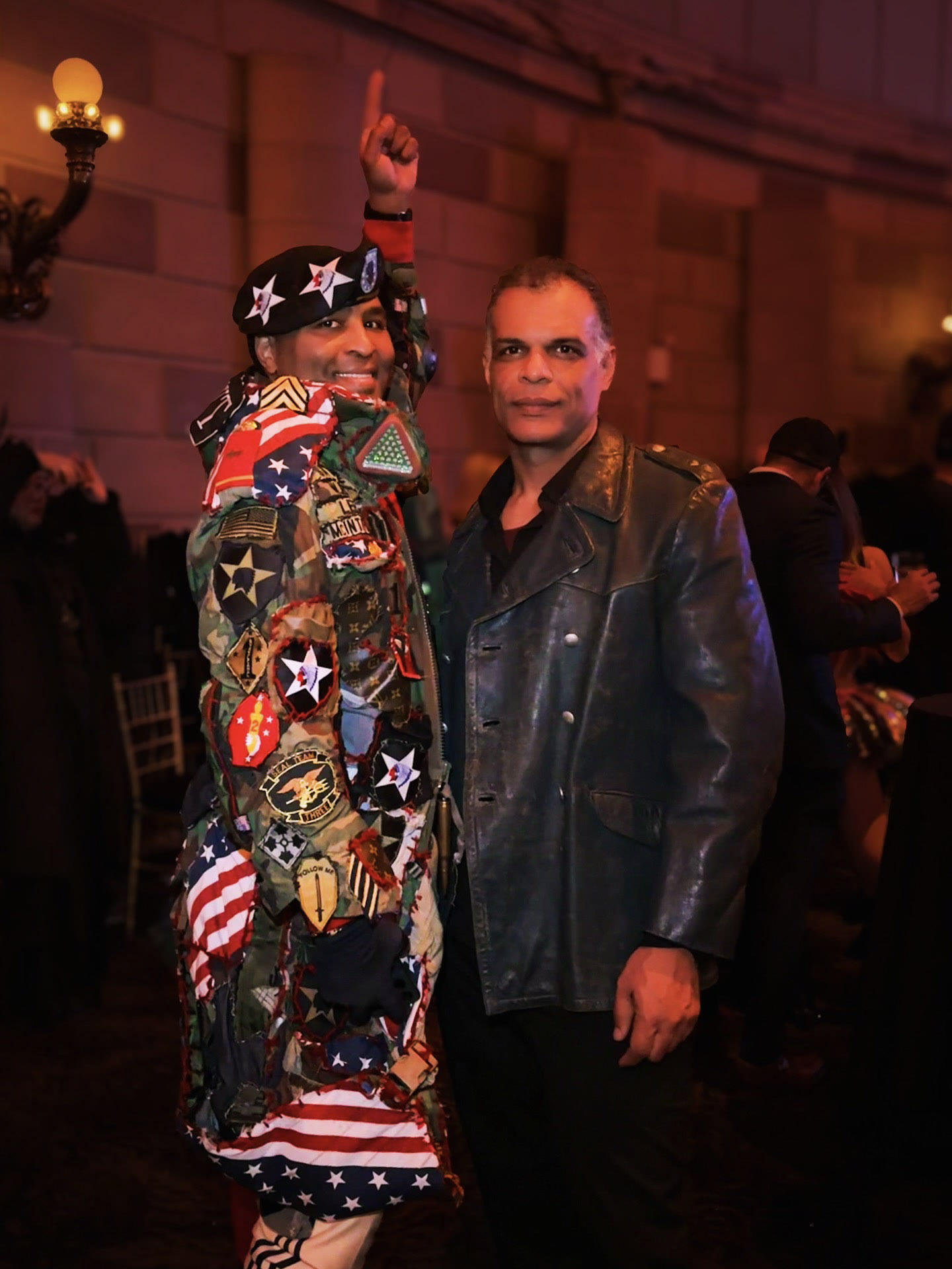 Kristopher in a leather jacket beside another guest in a colorful outfit at a fashion event.