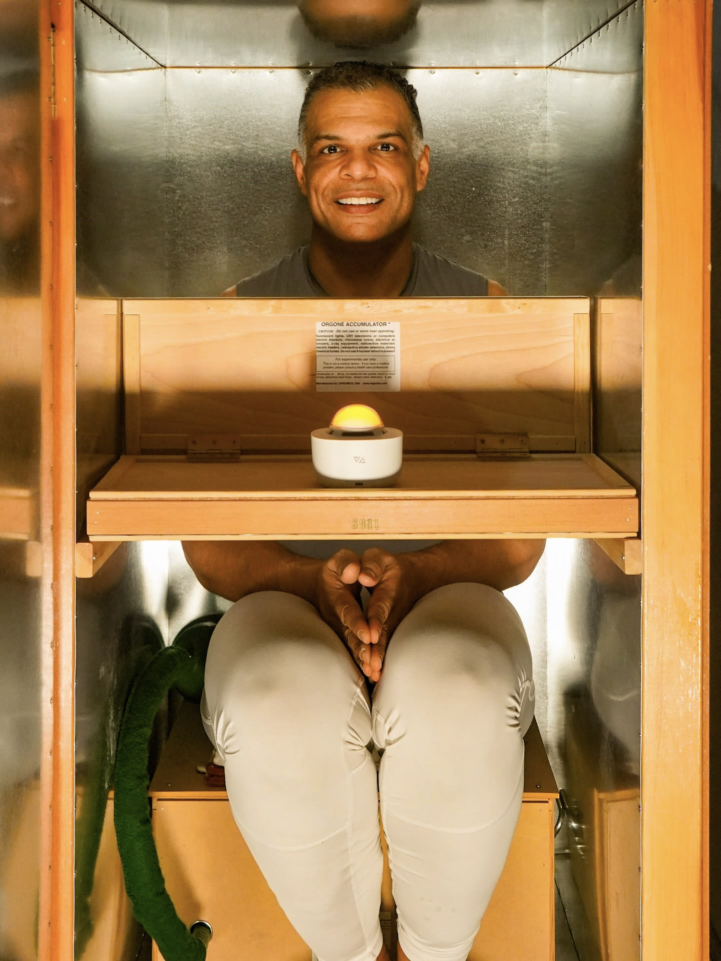 Kristopher smiling through a square opening in a wooden wellness enclosure.