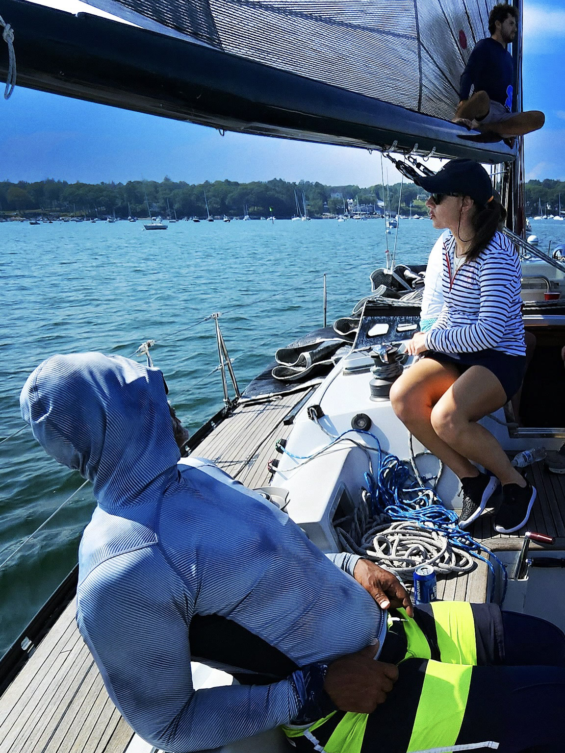 Two people aboard a sailboat on blue water.