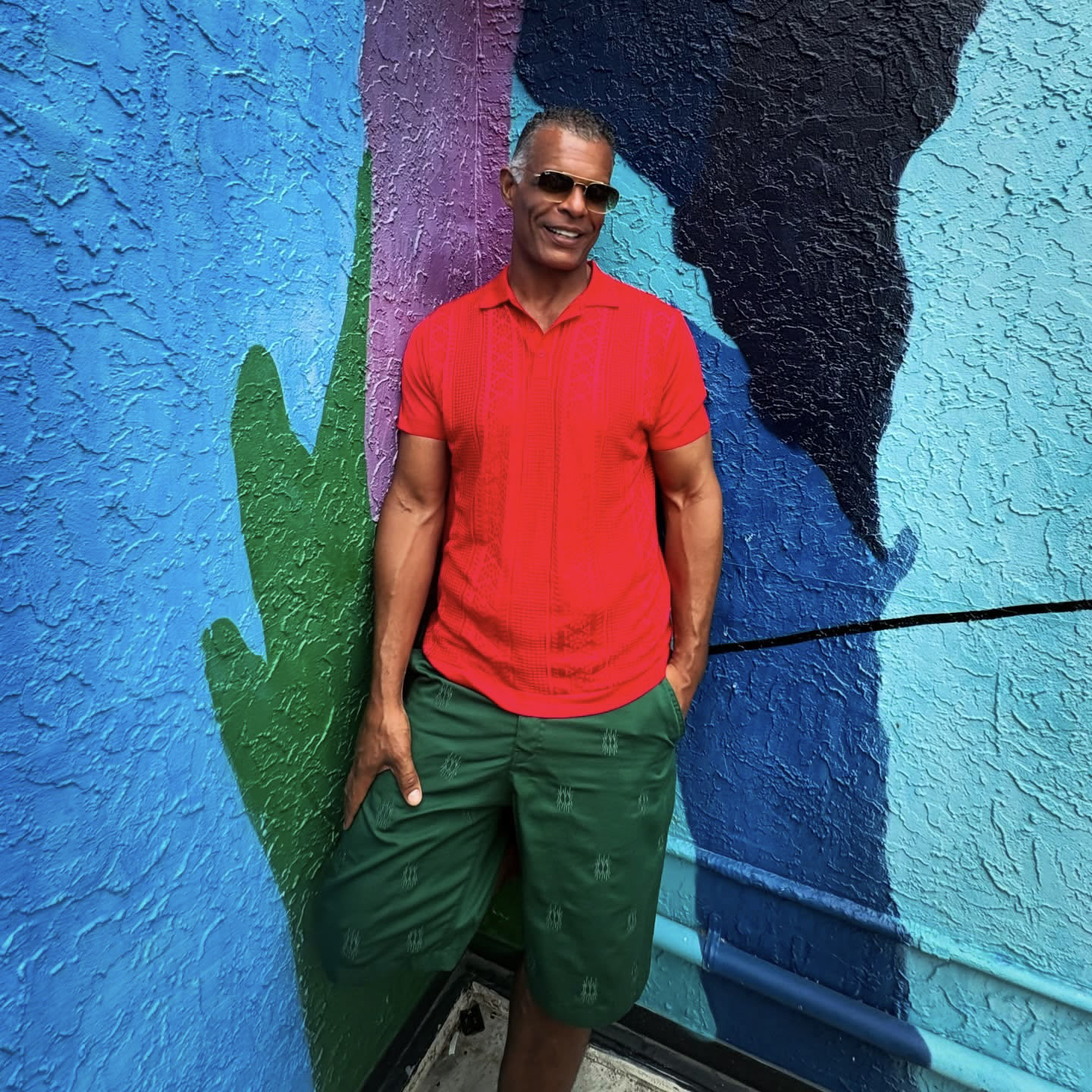 Kristopher in a red polo and green trousers beside a painted mural.