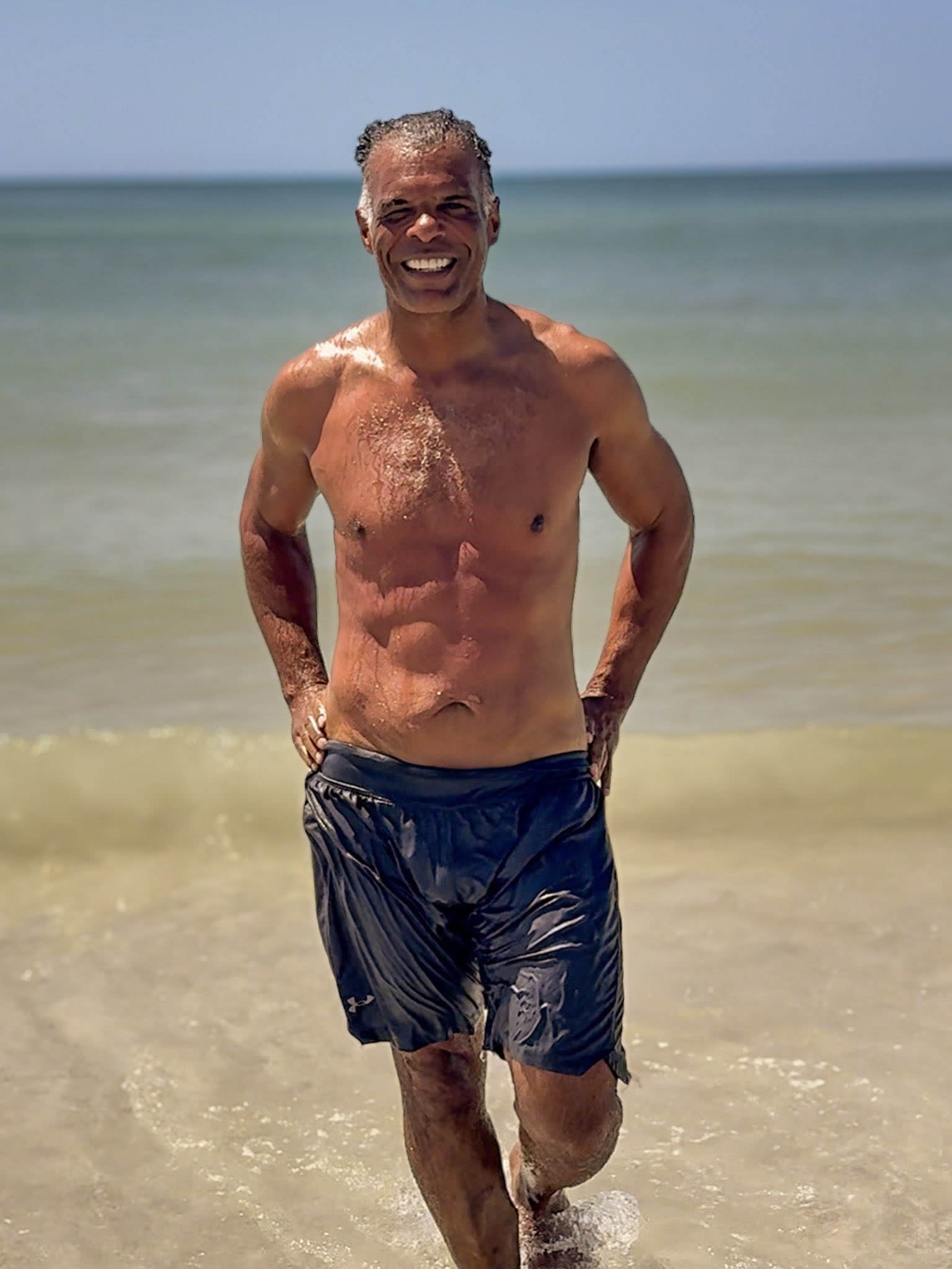 Smiling full-body beach portrait in dark shorts.