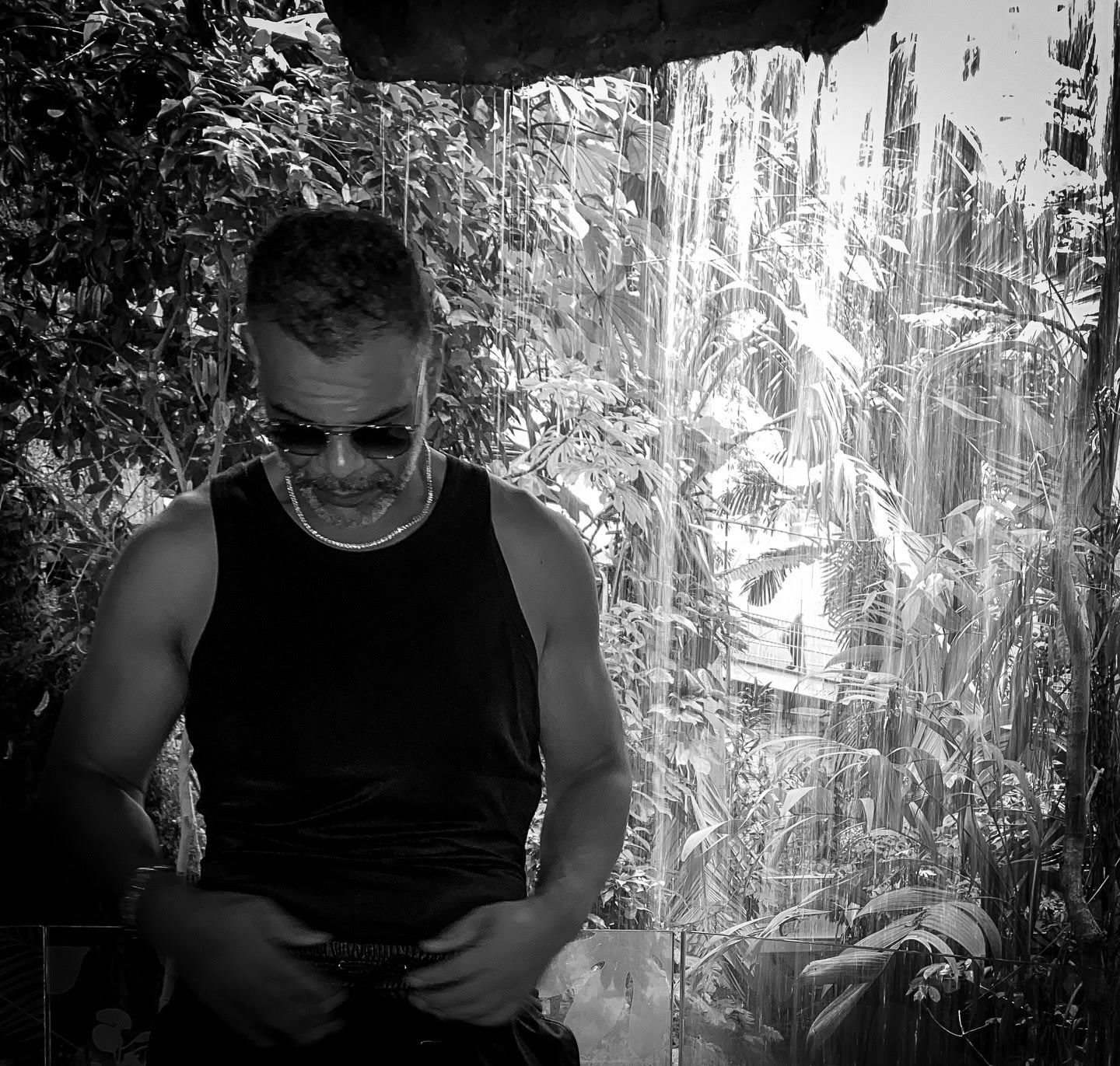 Black-and-white portrait of Kristopher seated outdoors beneath trees.