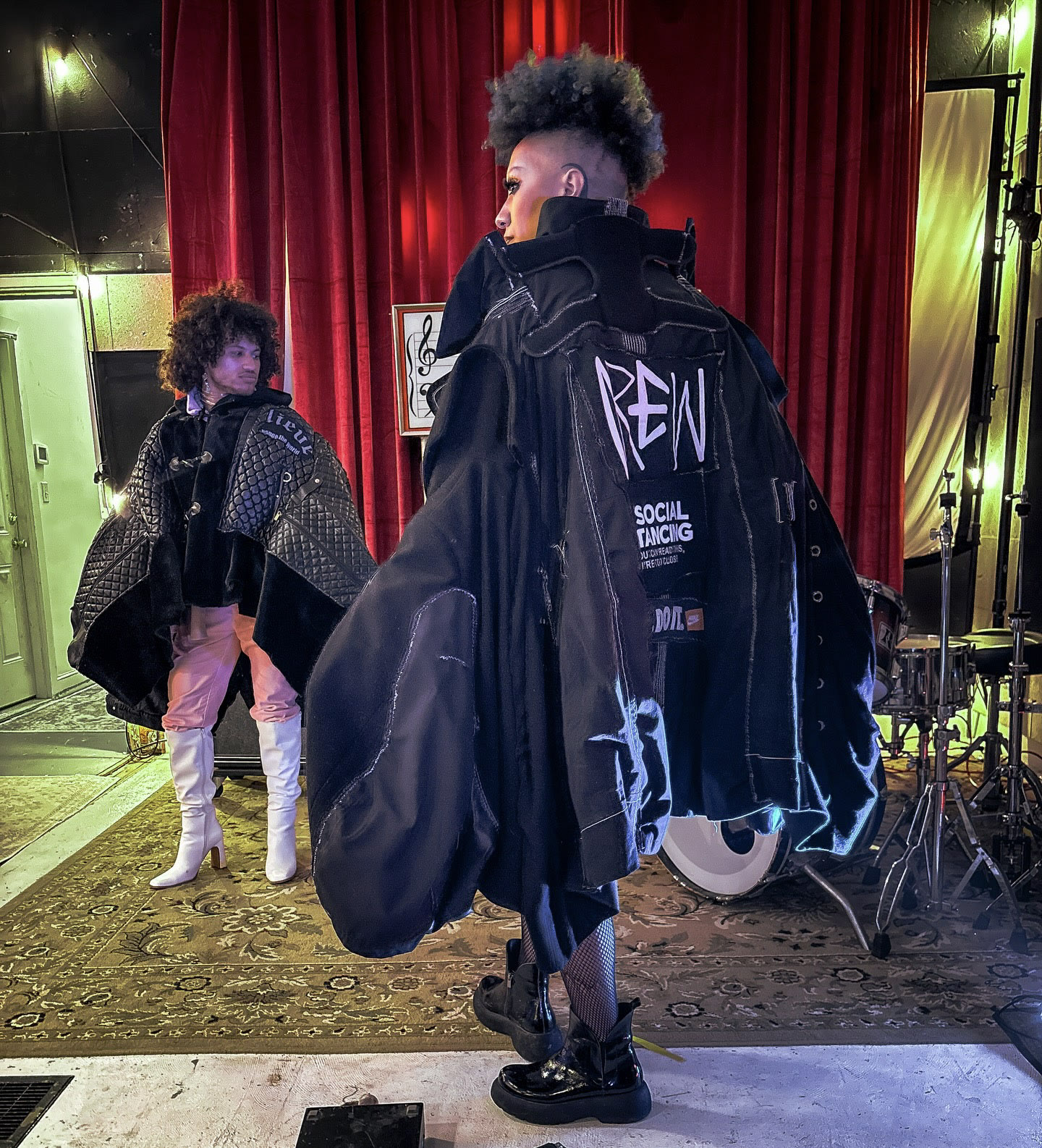 Performers wearing dark sculptural garments in a stage setting.