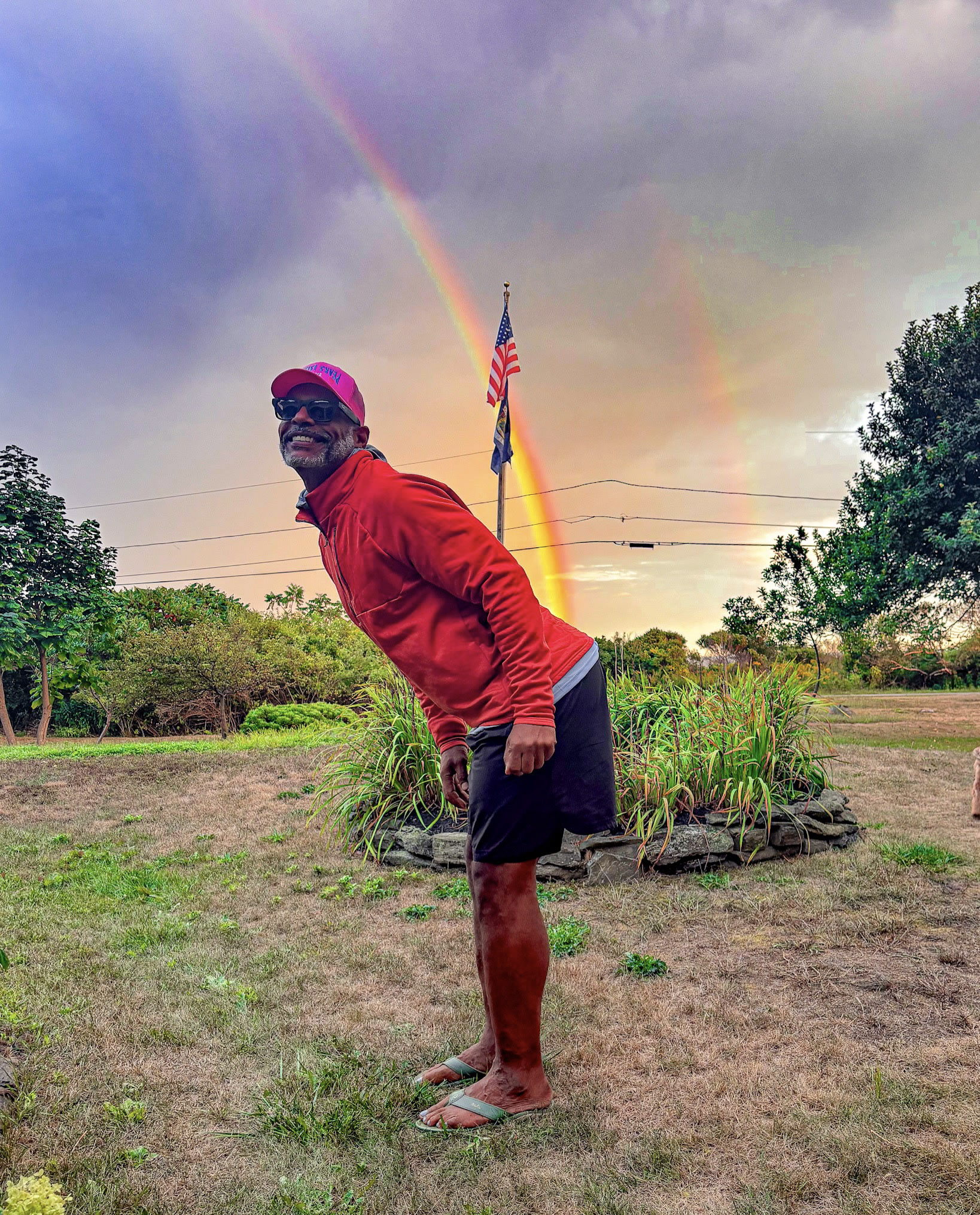 Kristopher in a red top outdoors beneath a rainbow.