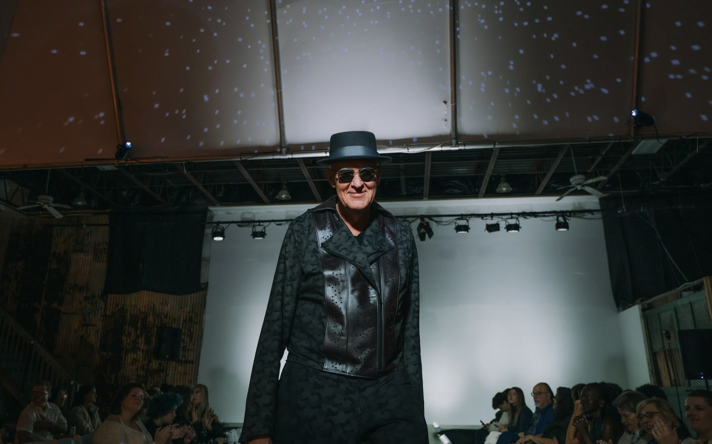 Kristopher on a runway in a dark outfit and hat.