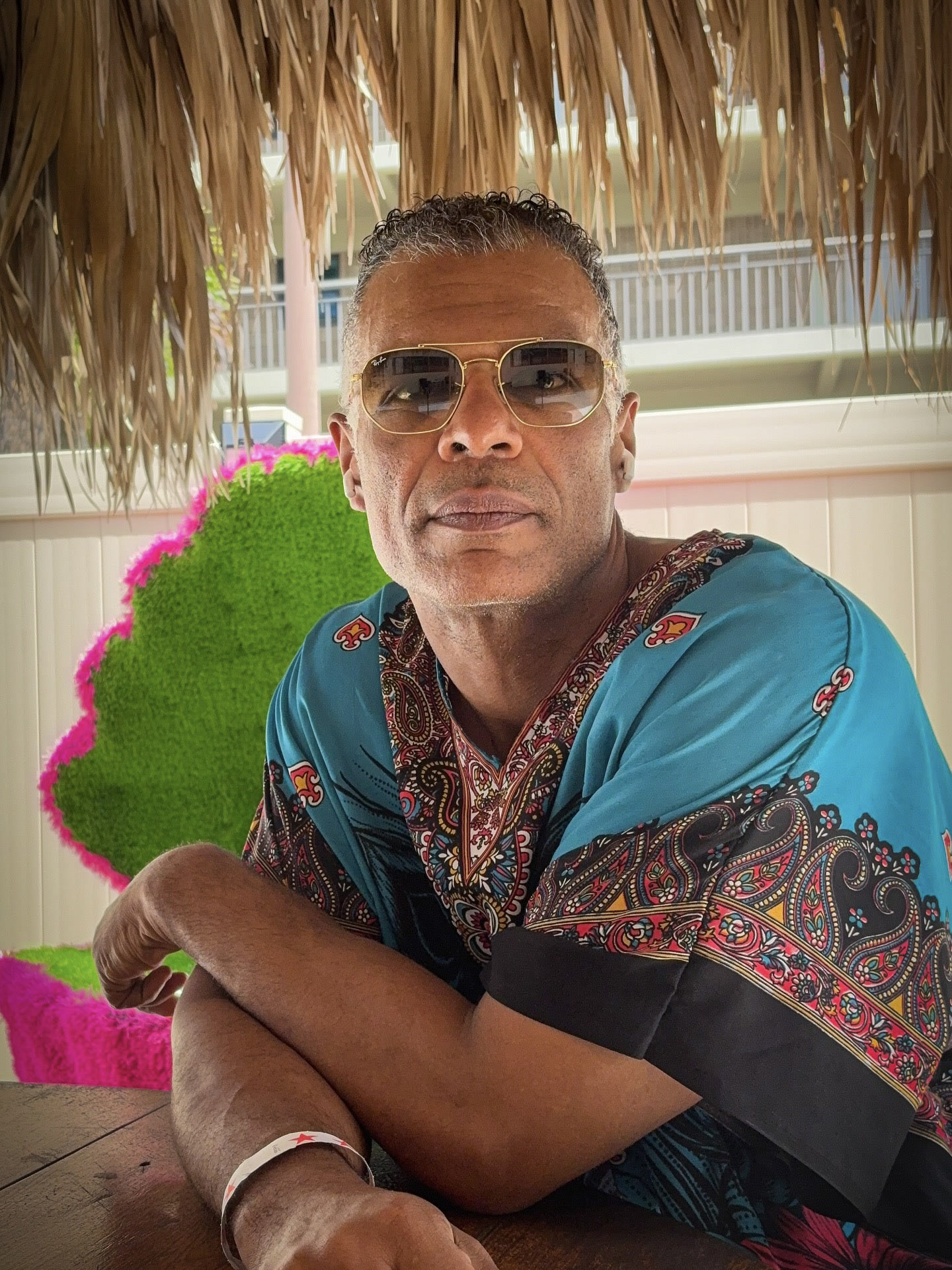 Kristopher seated under a thatched roof in a blue patterned shirt.