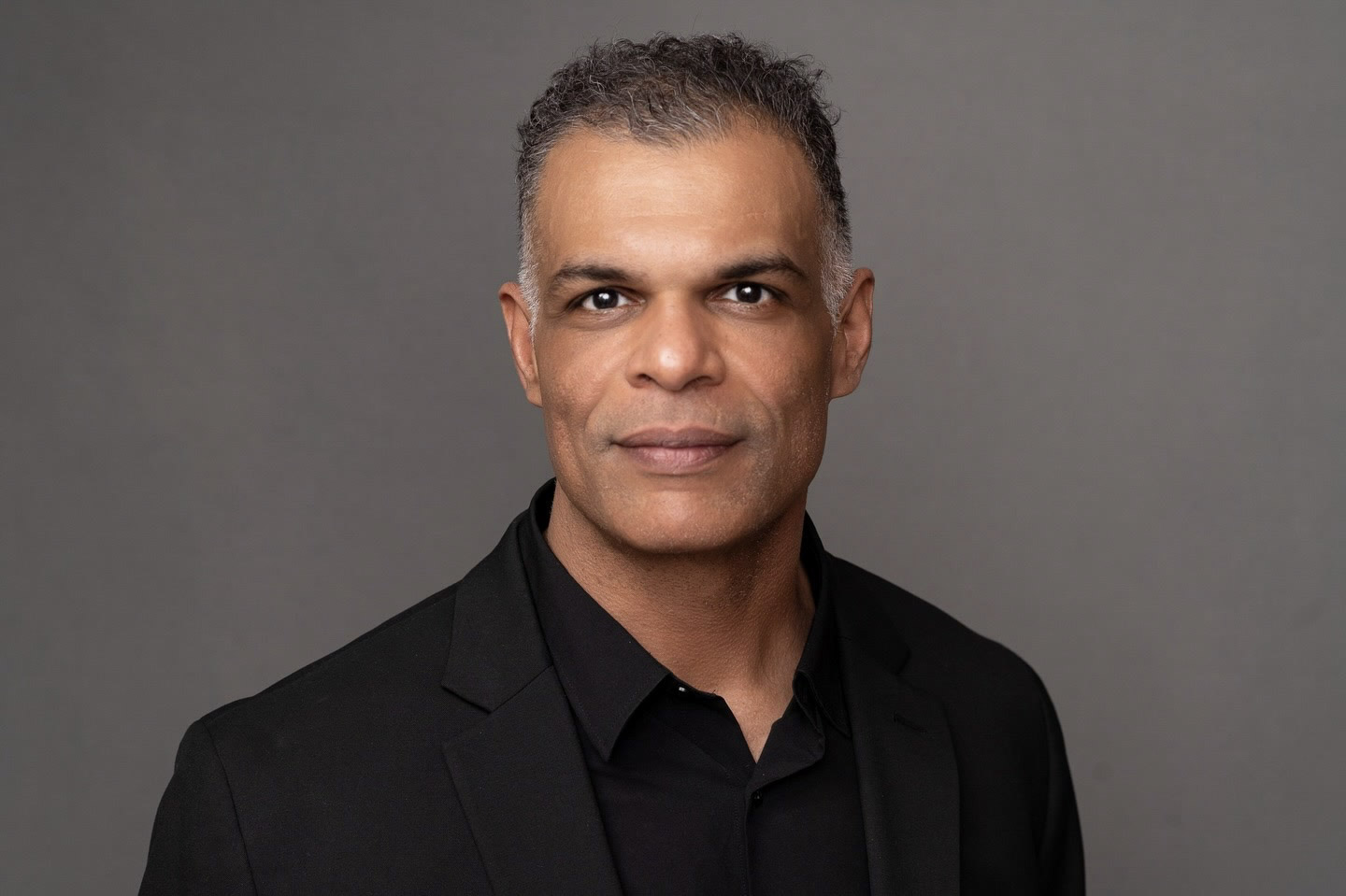 Studio-style headshot of Kristopher in a black collared shirt.