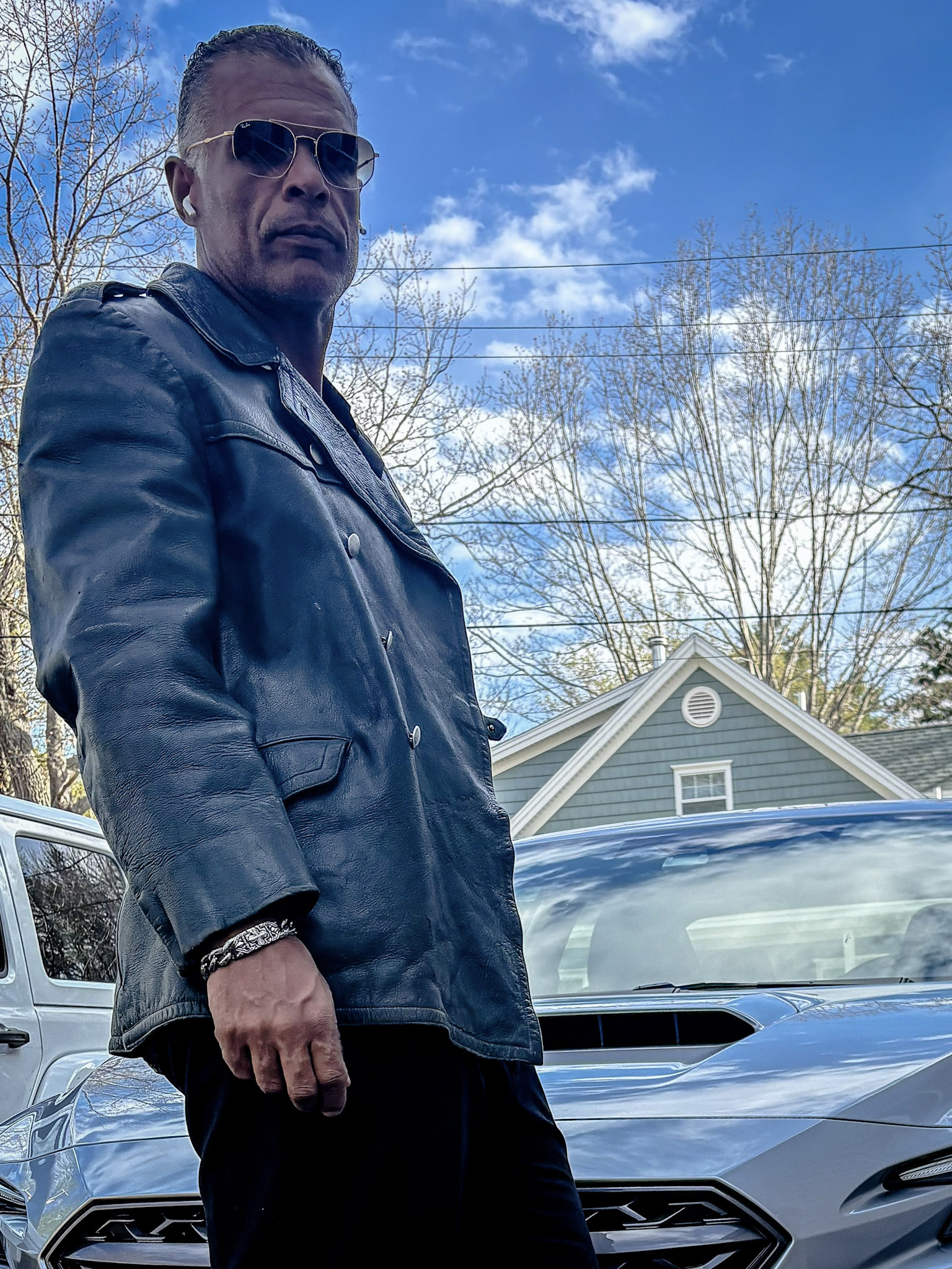 Kristopher wearing a blue-grey jacket outdoors beside a car.