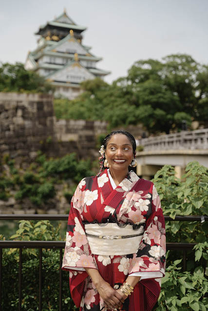 Woman in red floral kimono smiling with Osaka Castle in background