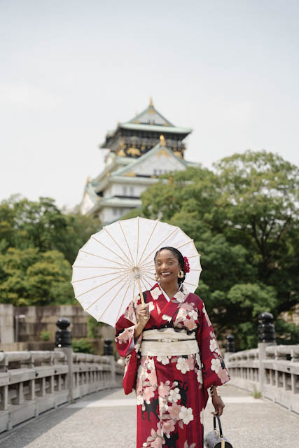 Woman in red kimono holding white parasol on bridge with castle background