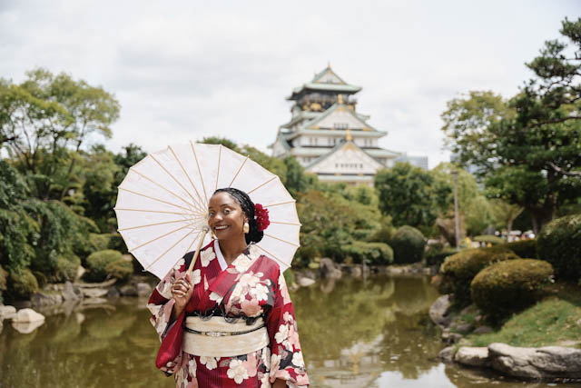Woman in red floral kimono holding white paper umbrella in Japanese garden