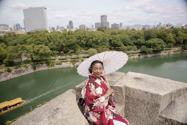 Woman in red floral kimono holding parasol sitting on stone wall