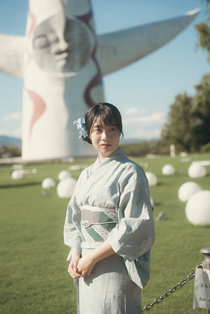 Woman in light blue kimono with flower hair accessory standing in front of large white sculpture