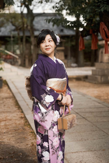 Woman in purple floral kimono holding traditional handbag standing outdoors