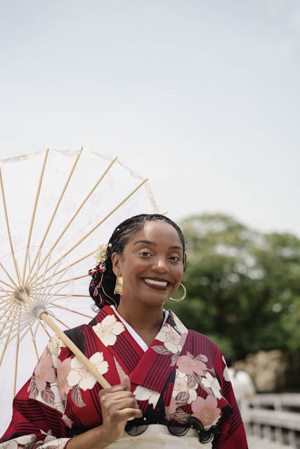 Smiling woman wearing red floral kimono holding traditional paper umbrella