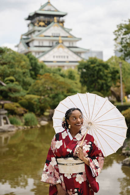 Woman in red floral kimono holding white paper umbrella in Japanese garden