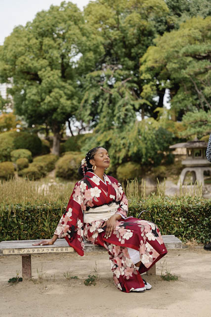 Woman in red floral kimono sitting on a wooden bench in a Japanese garden