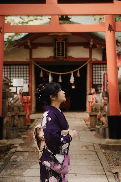 Woman in purple floral kimono looking up at red torii gate