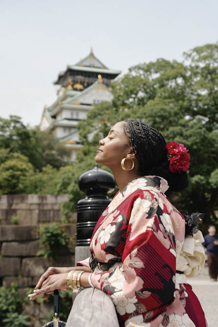 Woman in floral kimono with red flower in hair posing near castle