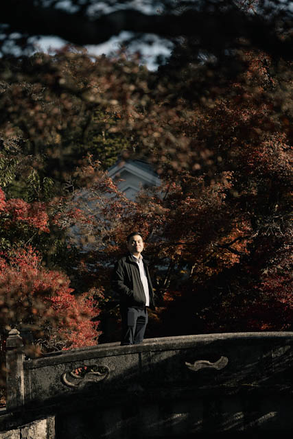Man standing on stone bridge amidst colorful autumn leaves