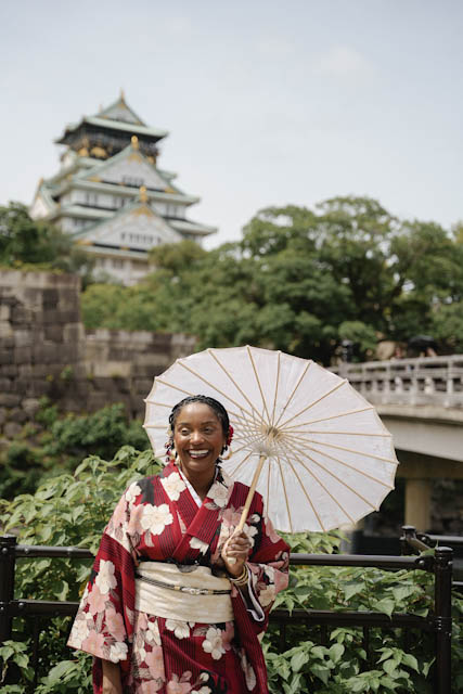 Woman in floral kimono holding parasol with Osaka Castle in background