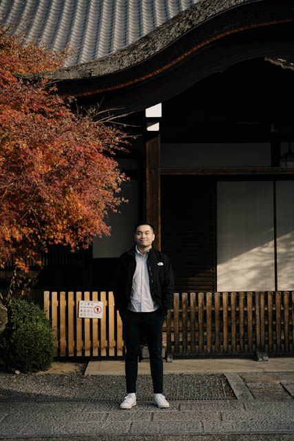 Man standing in front of traditional Japanese building with autumn foliage