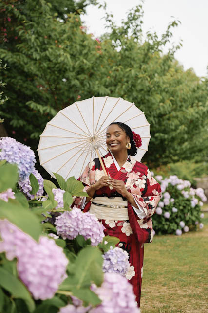 Woman in red kimono holding white parasol standing among purple hydrangeas
