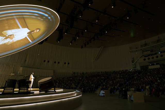 Speaker on stage with traditional drums and ceiling projection