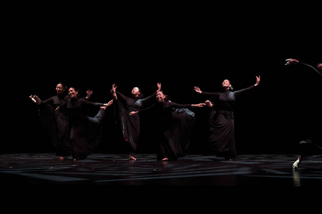 Dancers performing contemporary dance in black costumes on a dark stage